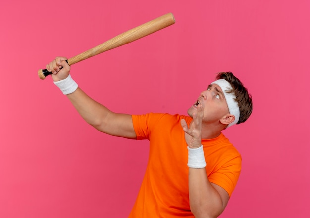 hombre deportivo guapo joven asustado diadema munequeras sosteniendo bate beisbol manteniendo mano aire mirando arriba aislado pared rosa 141793 94332
